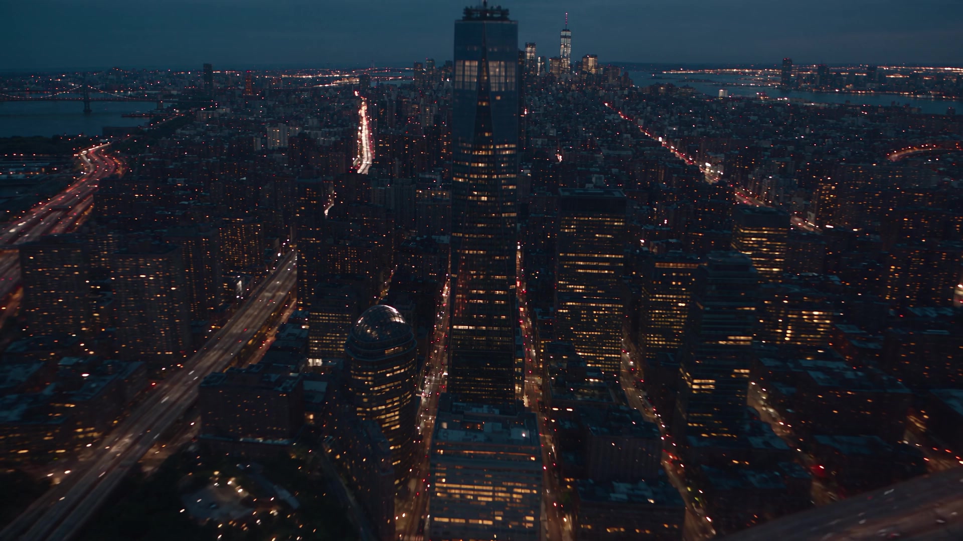 A city seen from above at dusk, its arteries lit